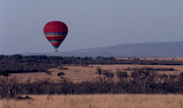 A hot air baloon flies over a rather dry Maasai Mara.